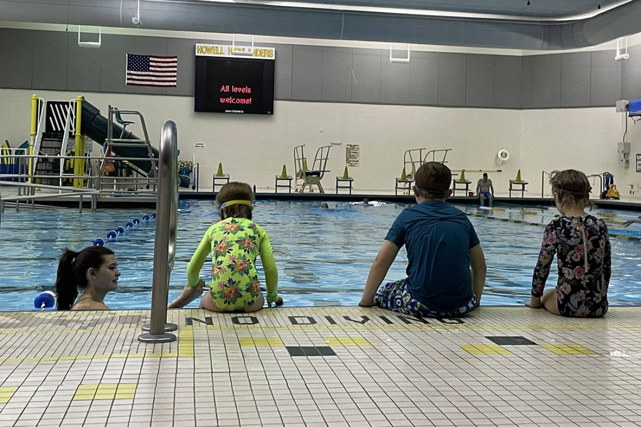 back of three students while they sit at the edge of the pool