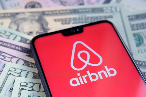 Airbnb app logo seen on the screen of smartphone, placed on dollar bills.
