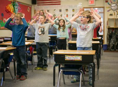 Students singing in a classroom with their hands in the air
