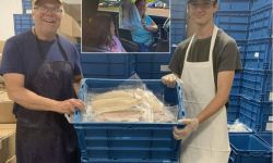 Workers pose with a crate of whitefish. Enbridge Energy and Massey Fish Company partnered to distribute free whitefish to area seniors, drawing cheers from allies and jeers from opponents who question the motives behind the company’s generosity. 