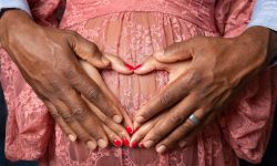 Hands of young African American black couple forming a heart shape on the pregnant belly of the woman with man's hands on top 
