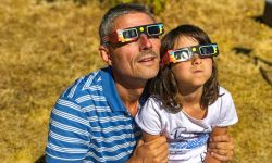 Father and daughter, family viewing solar eclipse with special glasses in a park.