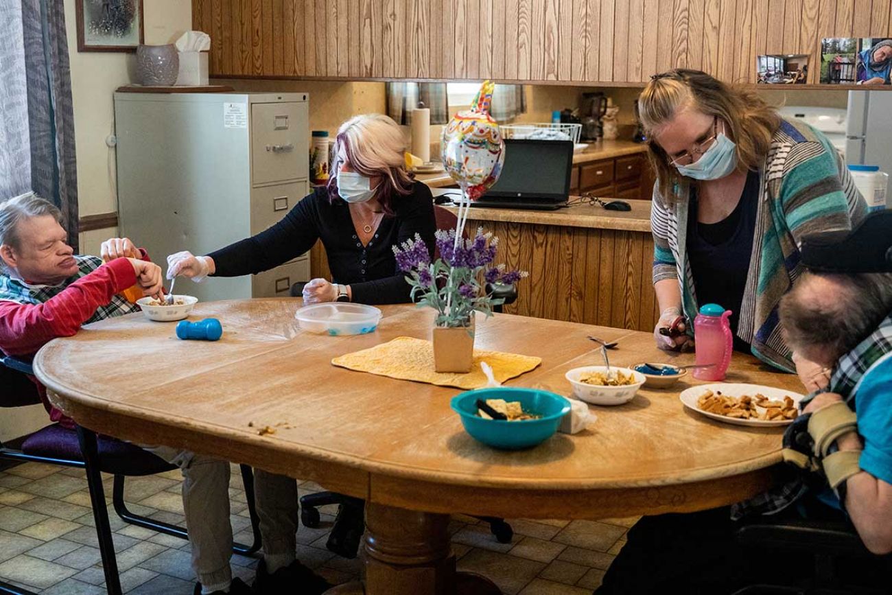 Holly VanVolkinburg, a supervisor, assists Larry Cook, 61, with lunch while Kathy Collier, Assistant Supervisor at MOKA, assists Stanley DeGlopper, 58, earlier this month at the Academy Home in Allegan.
