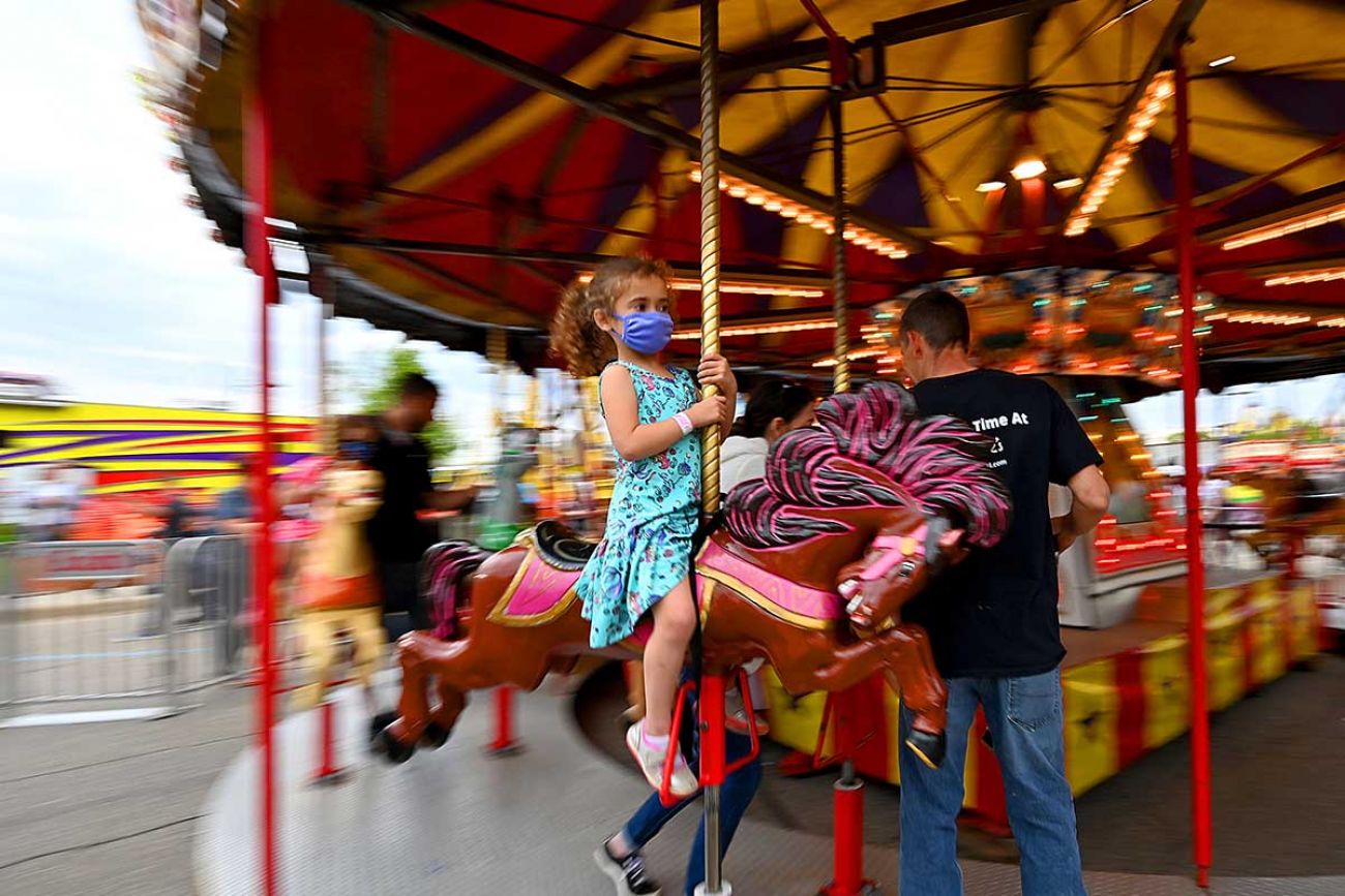 A young girl rides the merry-go-round while wearing a face mask
