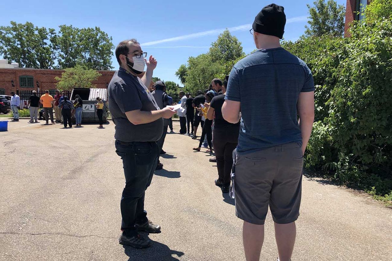 Jack Crawley of General Motors hands out codes for Flint Assembly job seekers to start their applications with their phones while they waited in line at a hiring event on June 17.