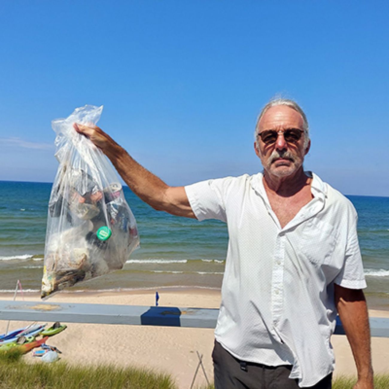 man holding a bag of trash, beach in the background