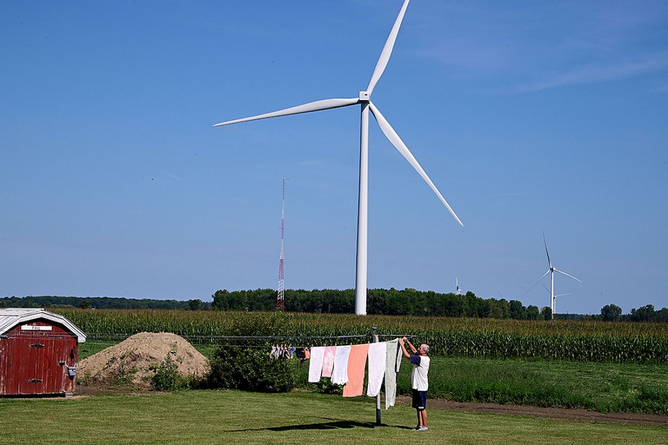man hanging up clothes with a wind turbine in the background