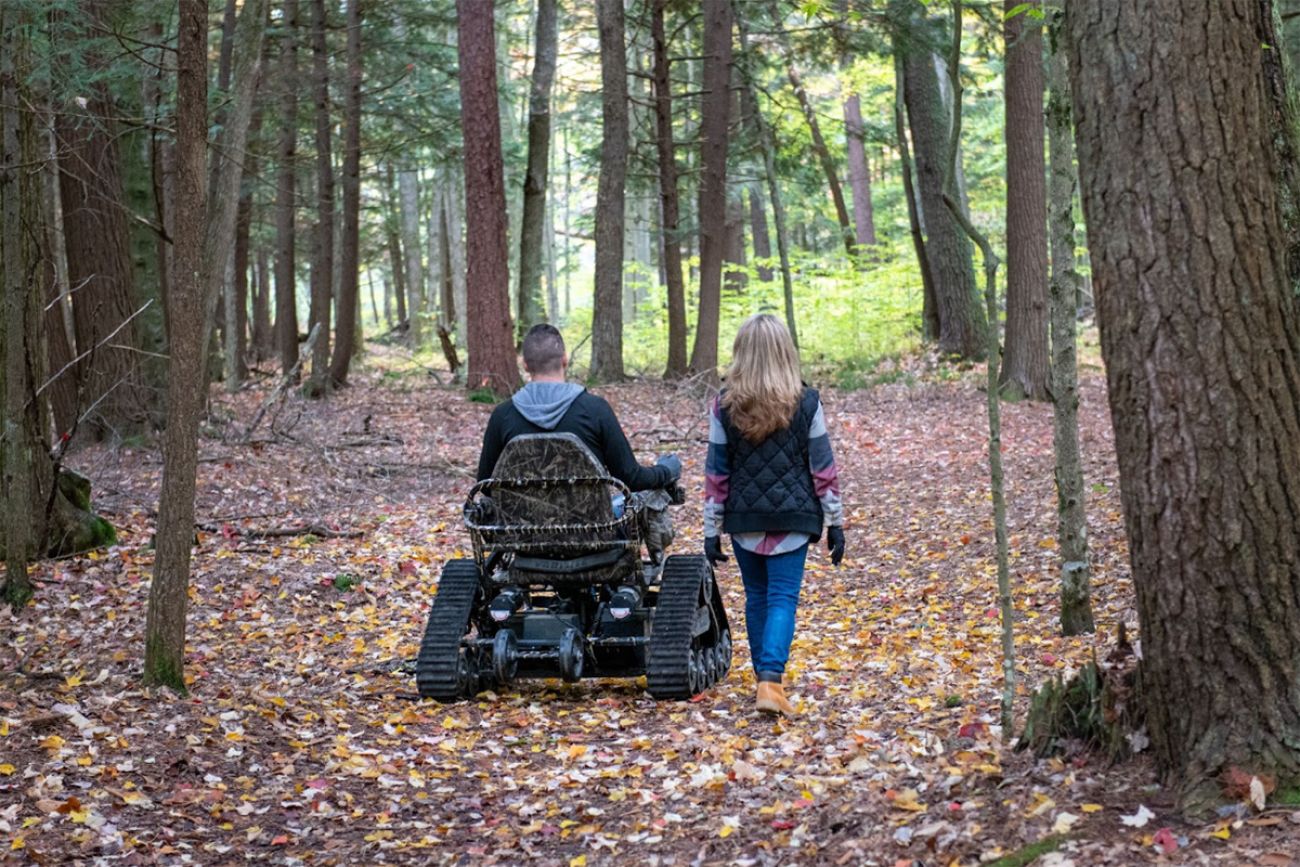 a person in an all-terrain wheelchair on a trail with a person walking beside them