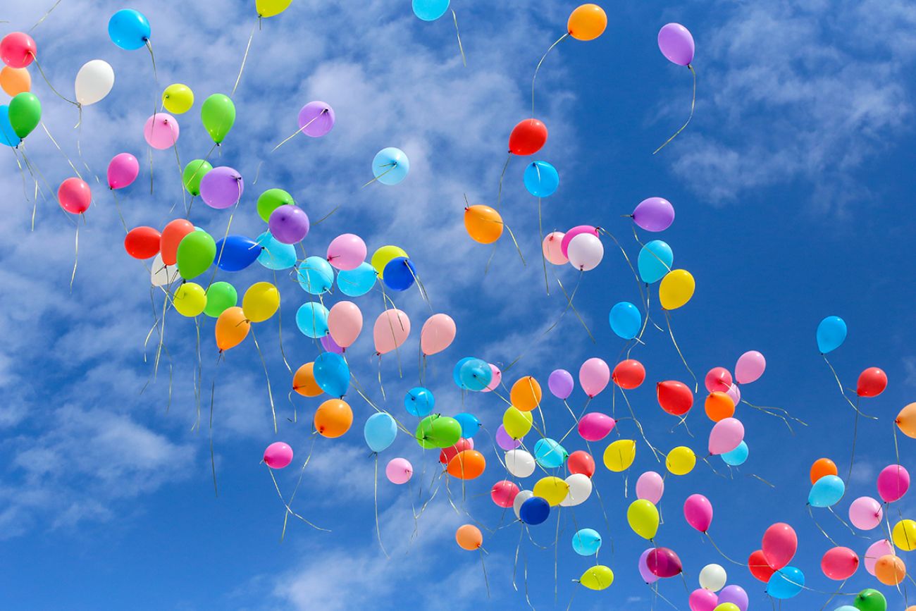 Multi-colored balls released into the blue sky.