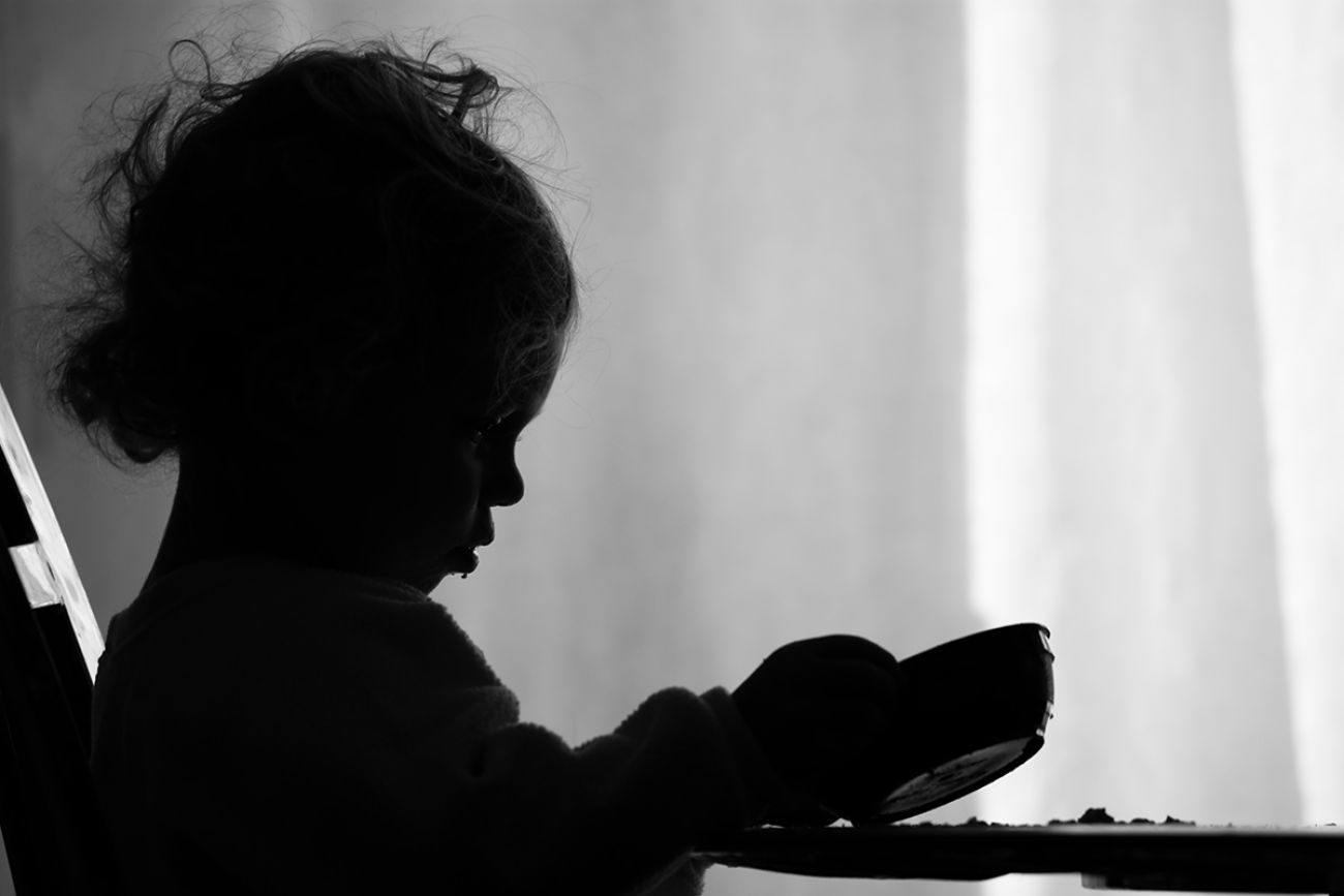 A two year old girl is sadly looking into her empty bowl wishing she had more to eat. 