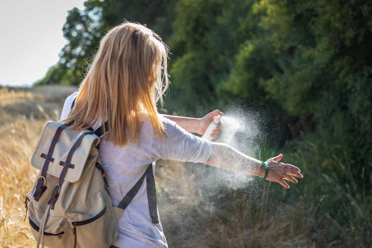 Woman applying mosquito repellent on hand during hike in nature