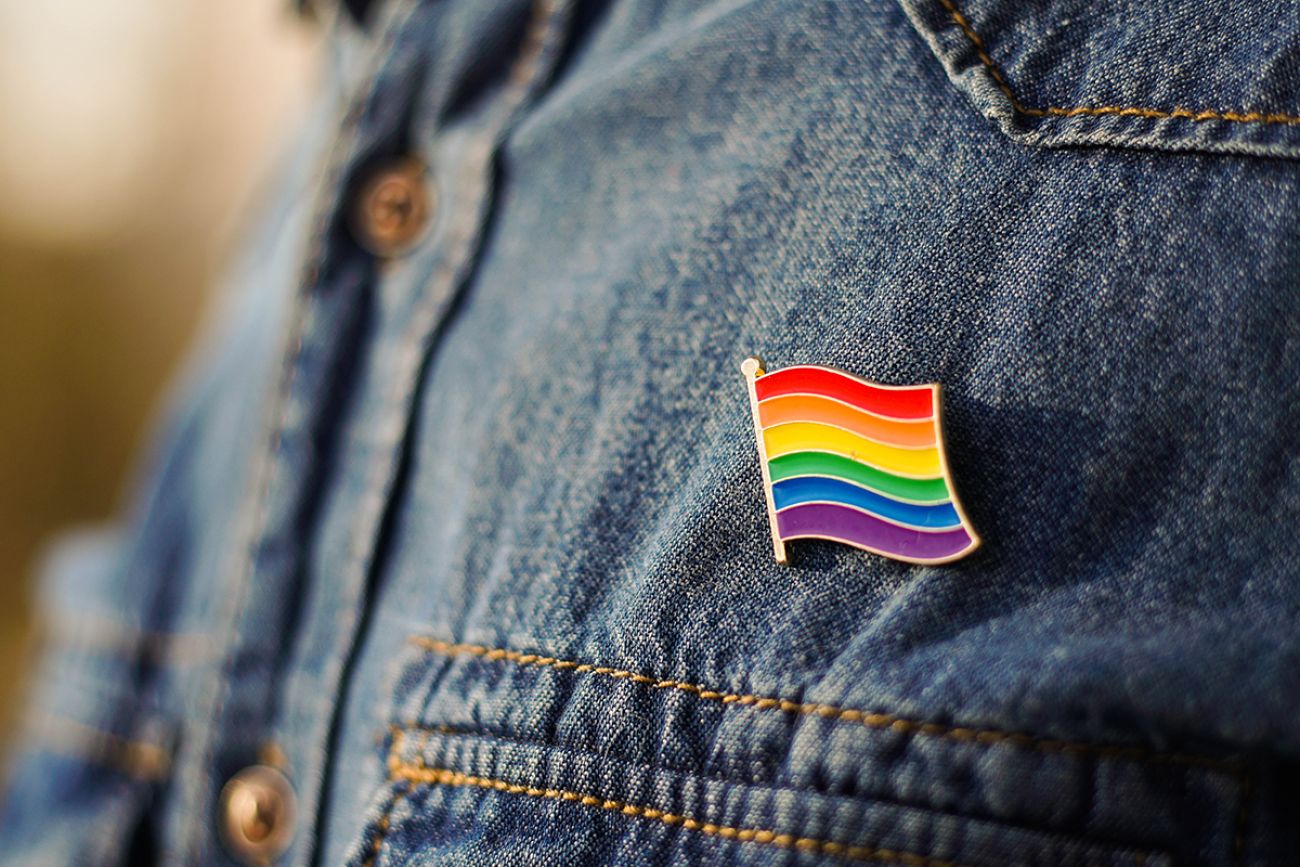 Close up of LGBT pin in the form of a flag is pinned on blue jeans jacket.