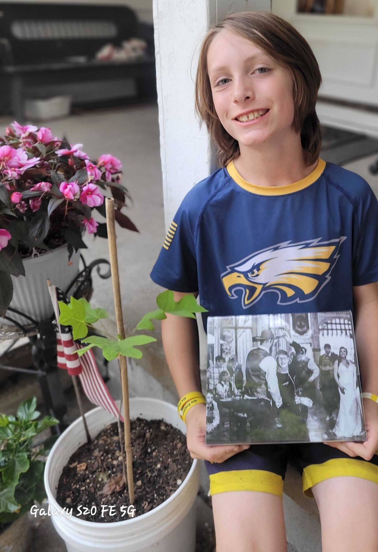 boy holding a photo next to a small tulip tree in a pot