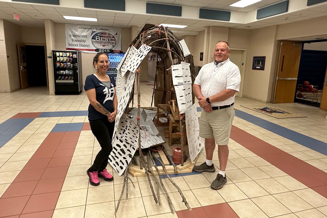two people standing next to a wigwam in a school lobby