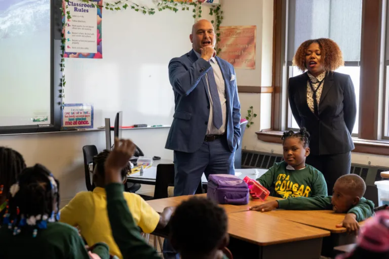 Two teachers stand in classroom in front of students