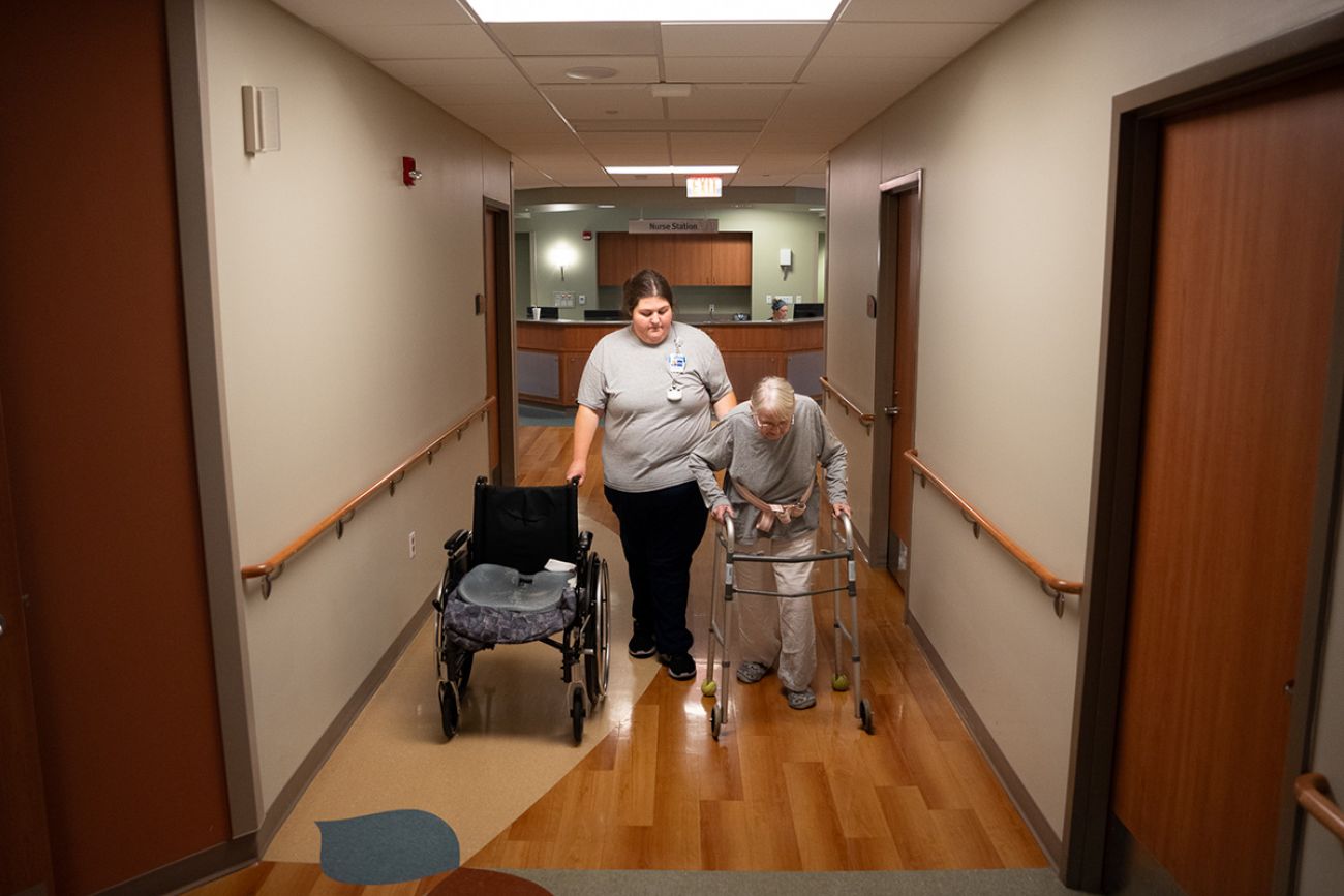one woman walking next to a woman using a walker in a hallway