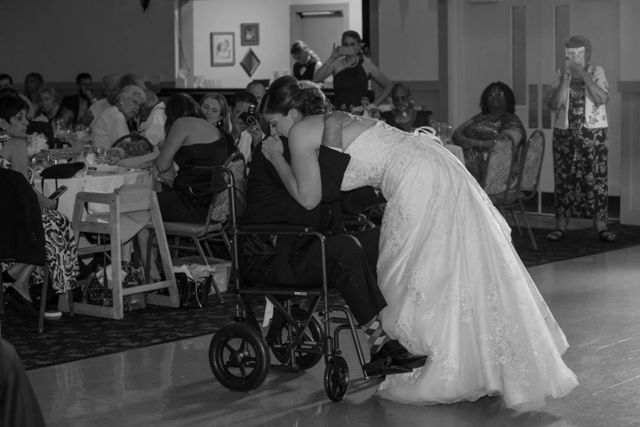 man in a wheelchair getting a hug from woman in wedding dress