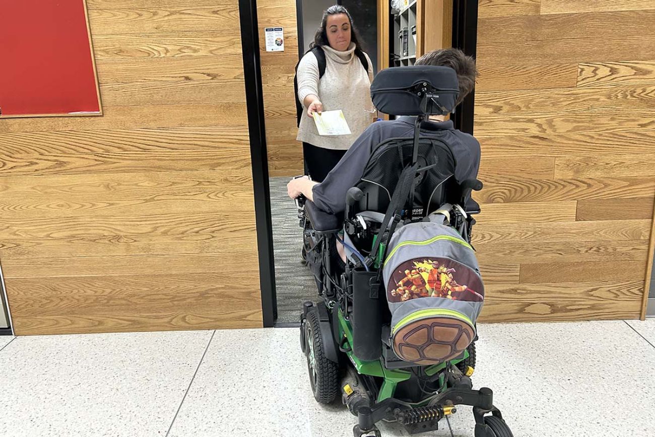 Emma Booth giving a piece of mail to a student in a wheelchair