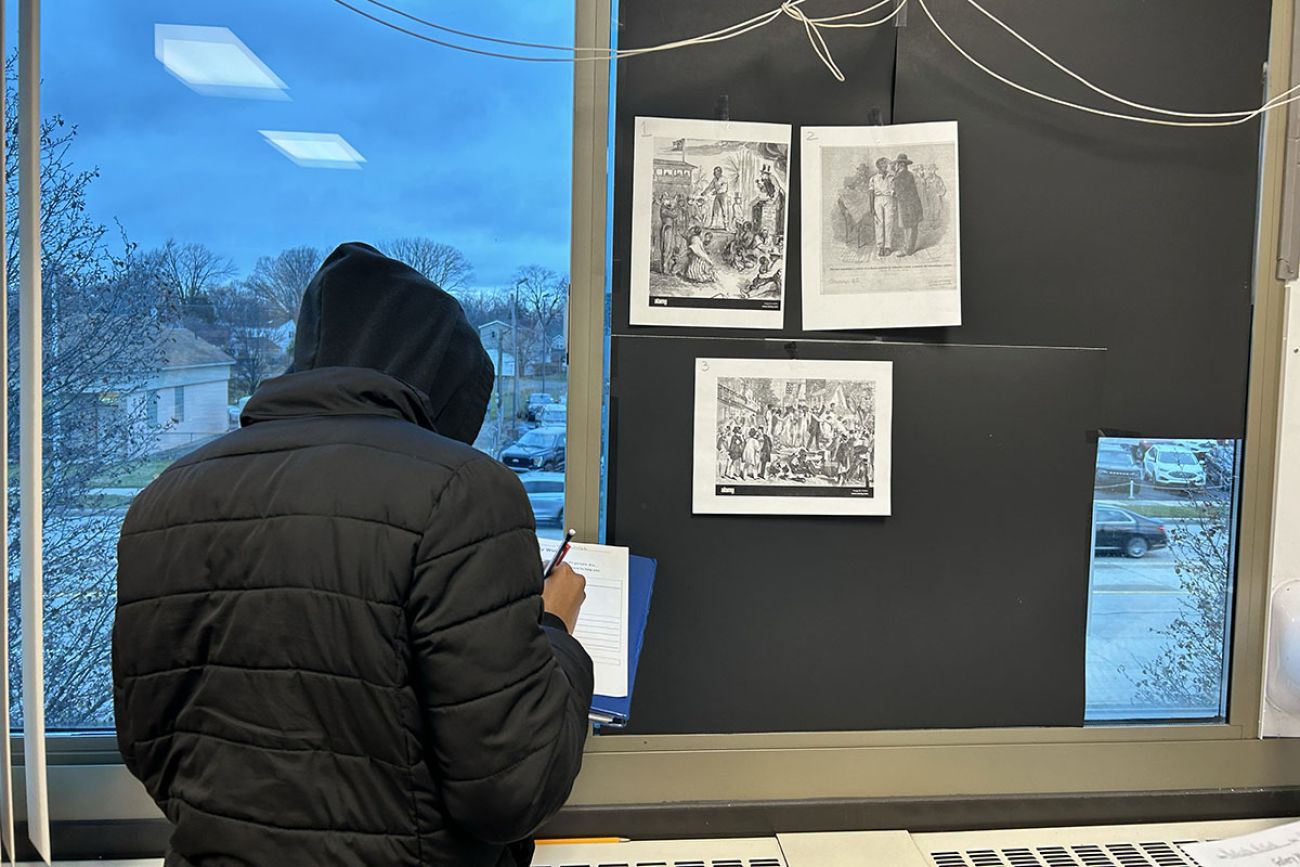 student writing in notebook, looking at photos