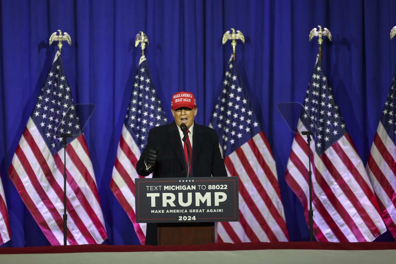 Donald Trump speaks at a podium with American flags behind him.