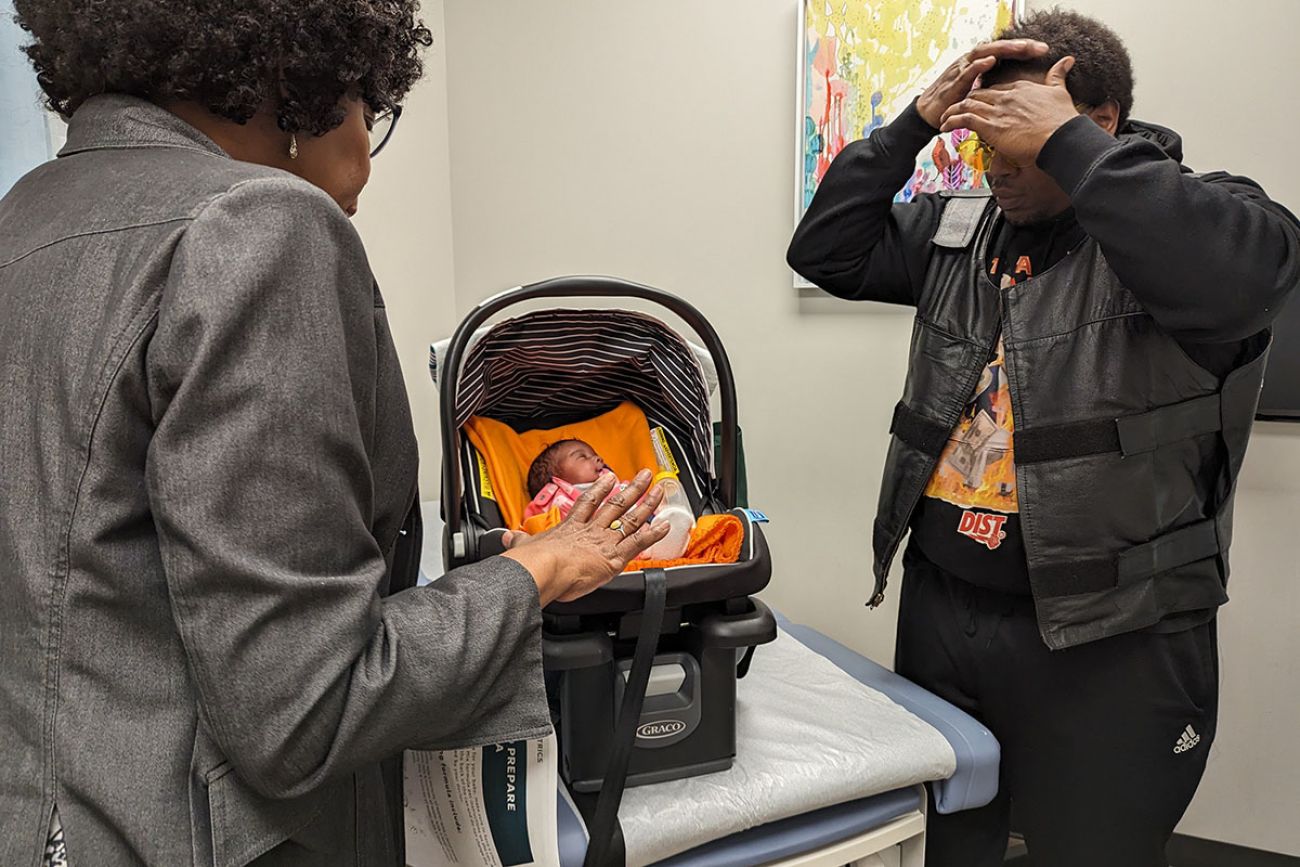 two adults in a doctor's office, with a baby in her carseat