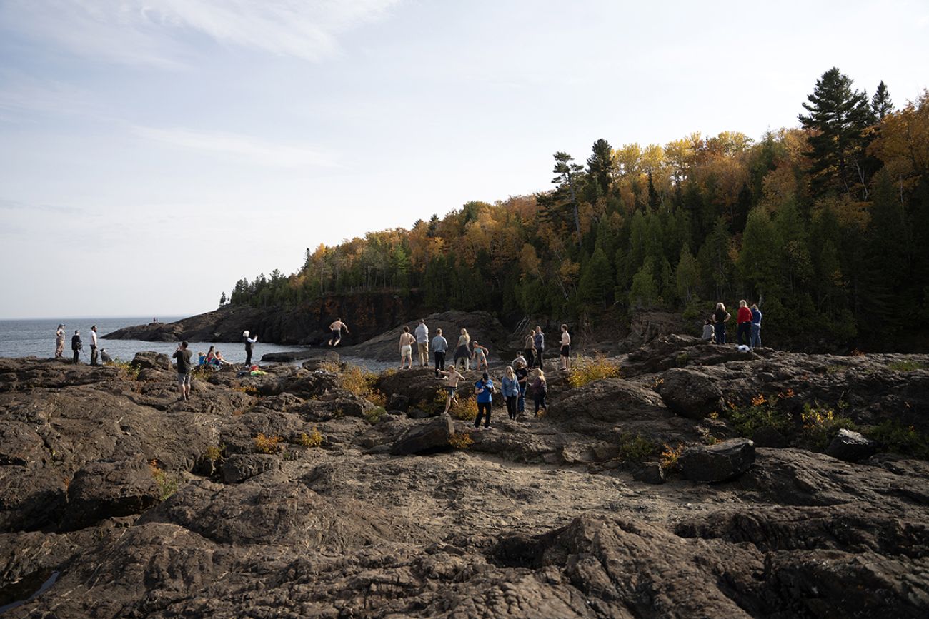 People standing, hanging out on dark-colored rocks at the Black Rocks at Presque Isle Park just north of downtown Marquette.