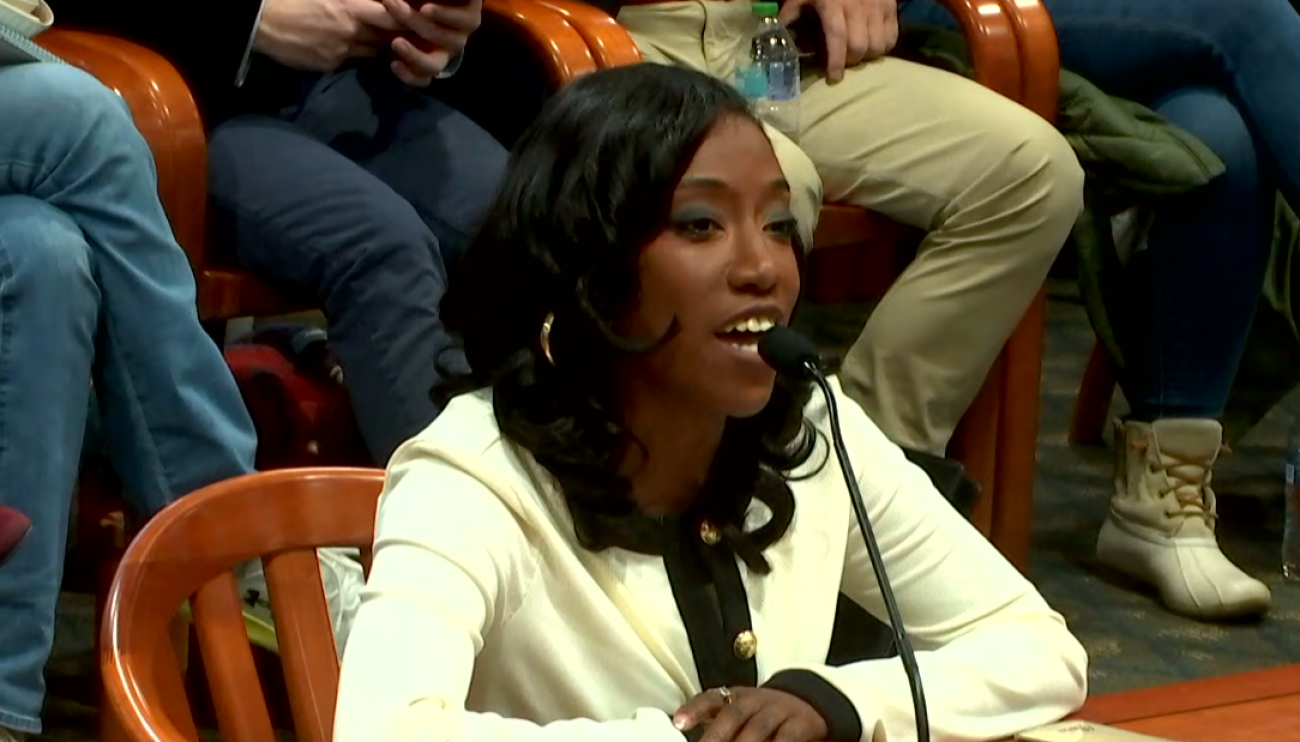 Charity Dean sits at a table with a microphone