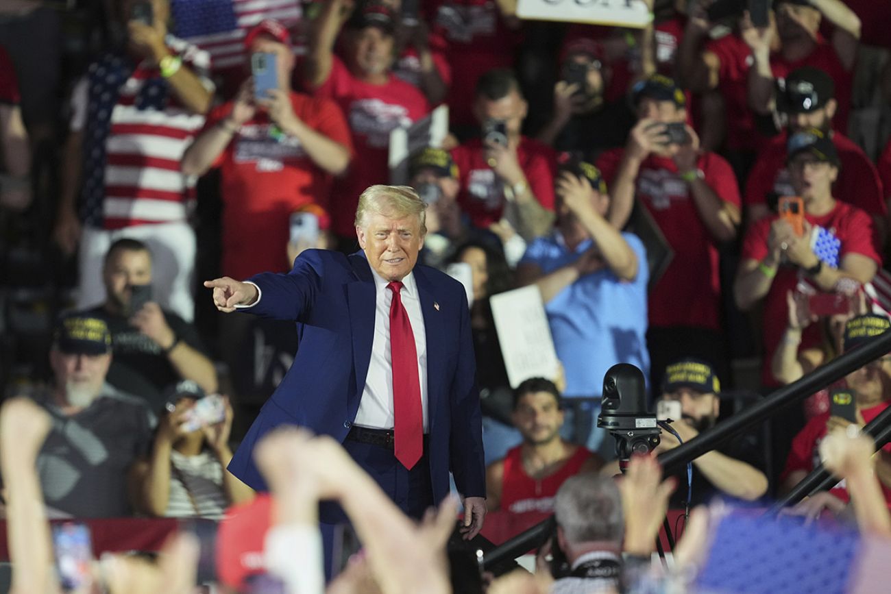 President Donald Trump walks on stage. People are behind him.