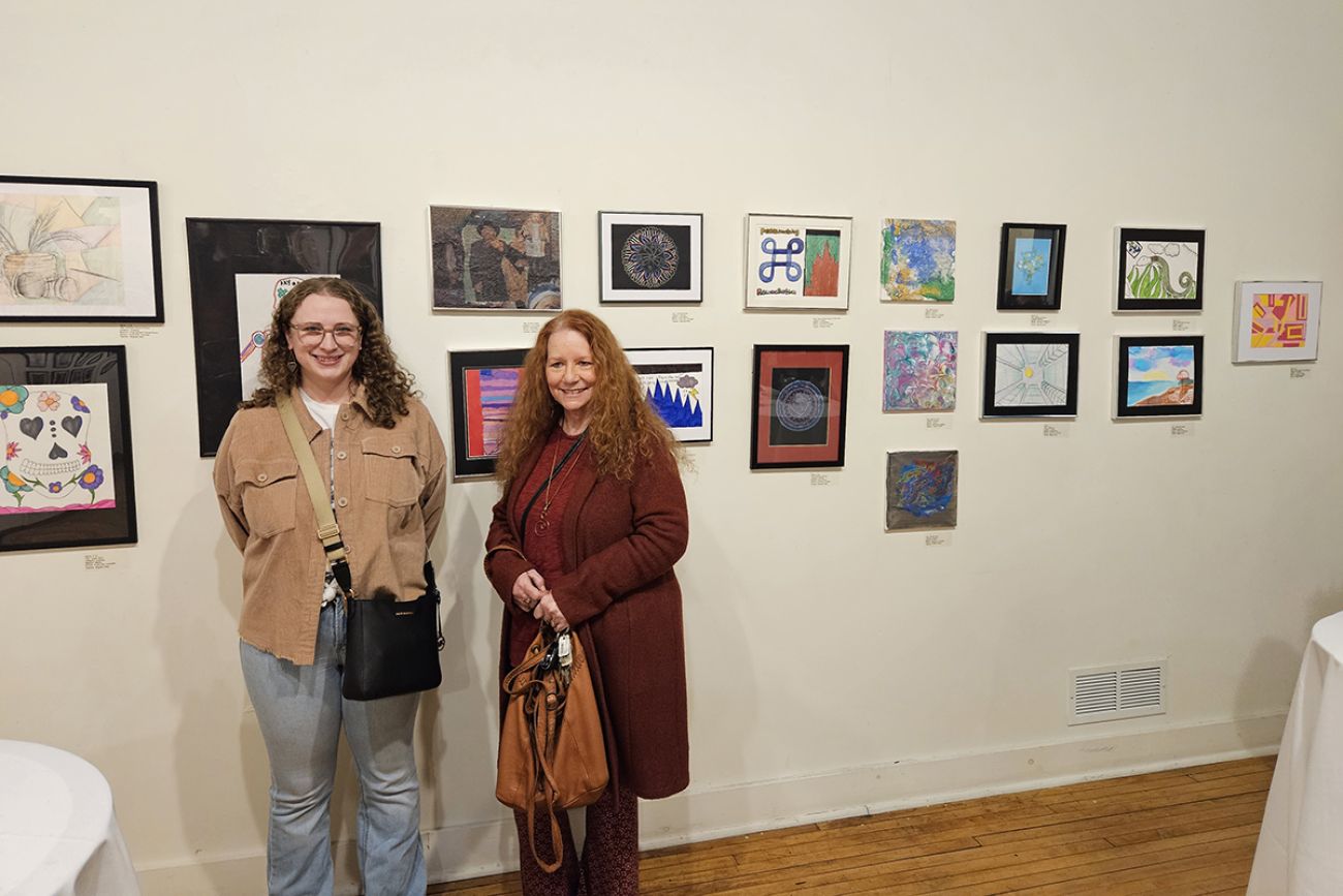 Meghan Kelly and Debbie Trombly pose in front of artwork on the wall behind them.