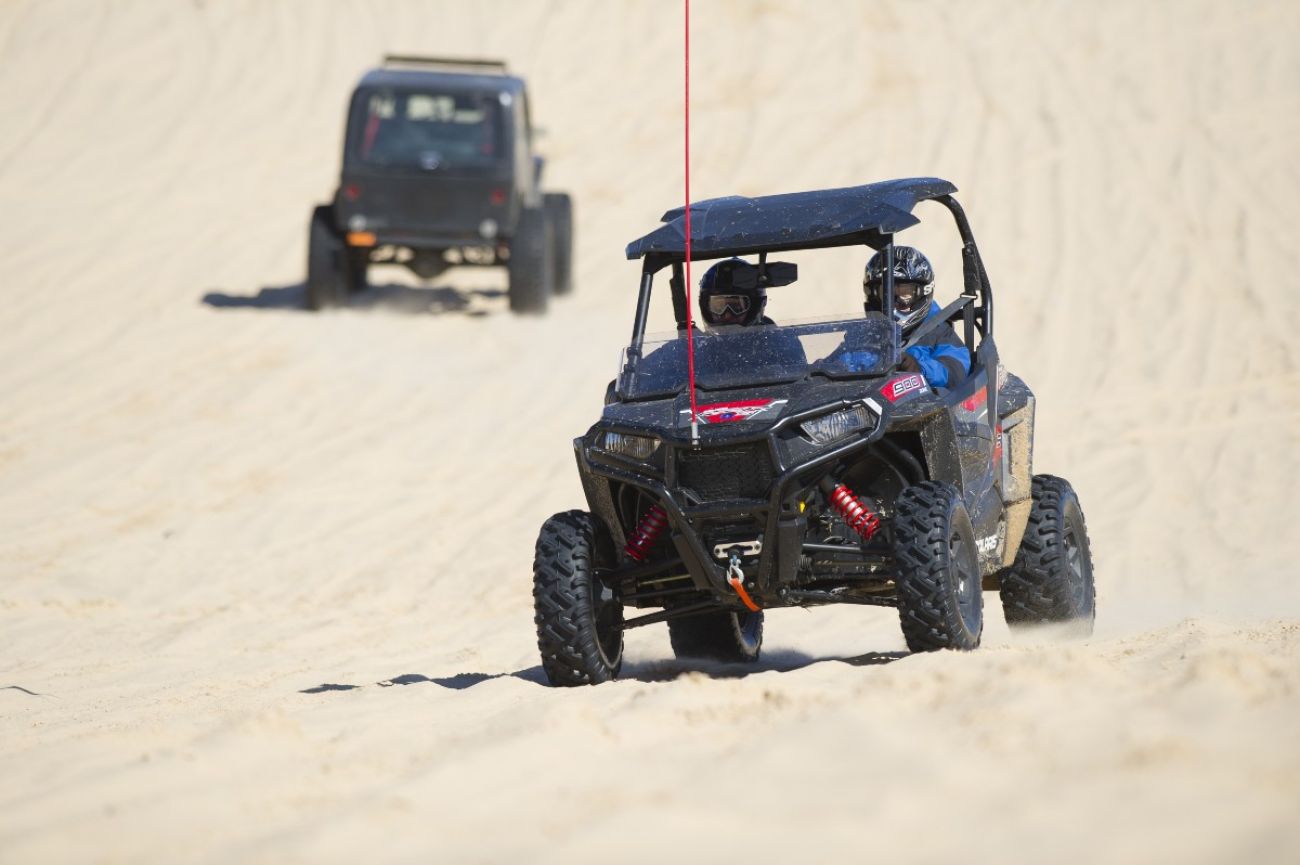 Two buggies drive around sand dunes