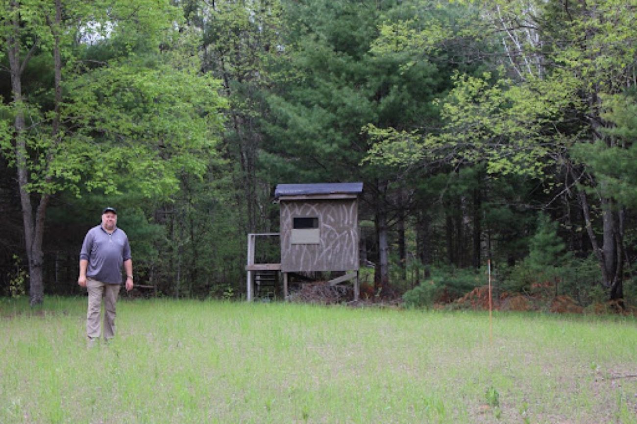 A man stands in a food plot next to a deer blind in northern Michigan