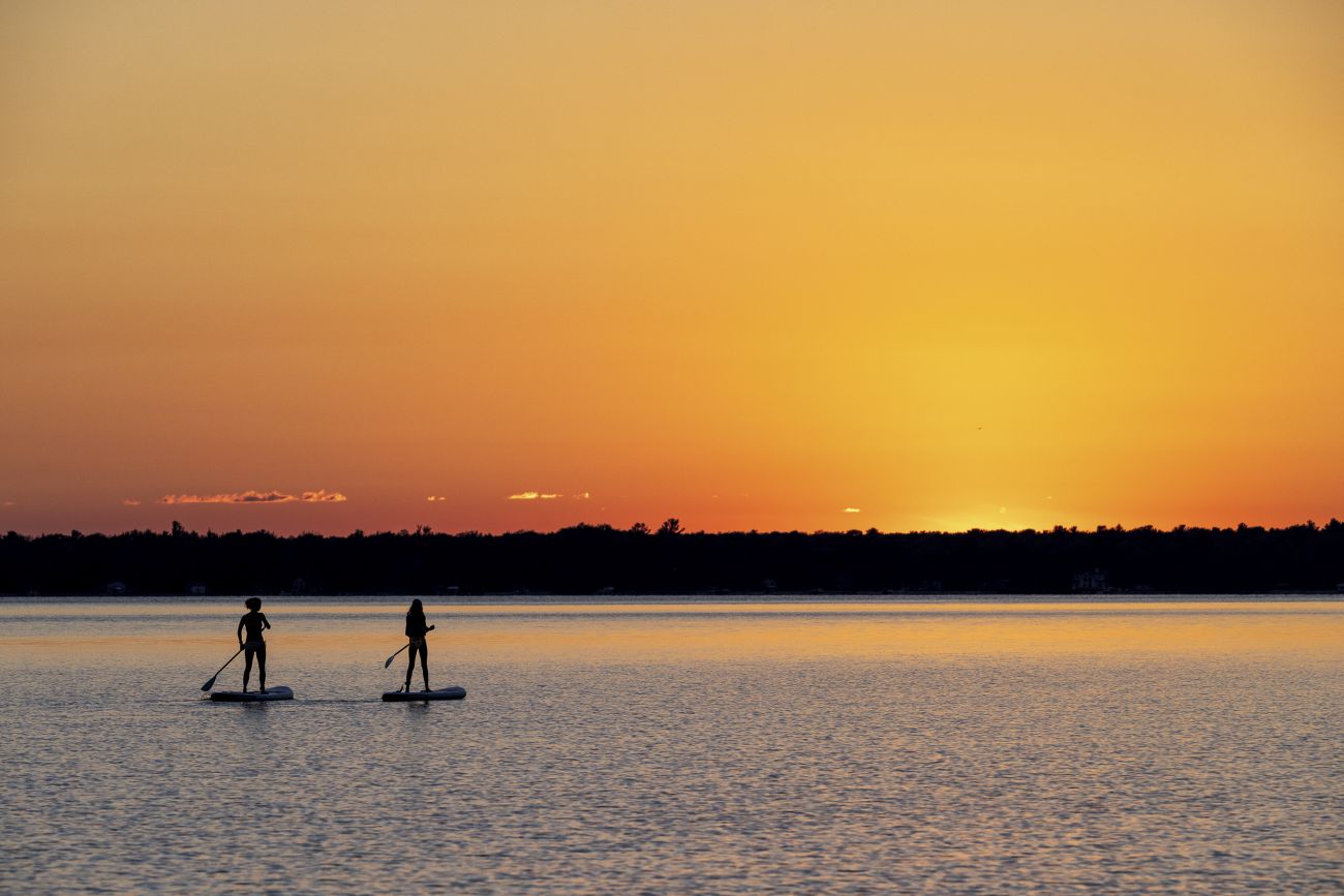 People are on a stand-up paddleboard on a lake at sunset.