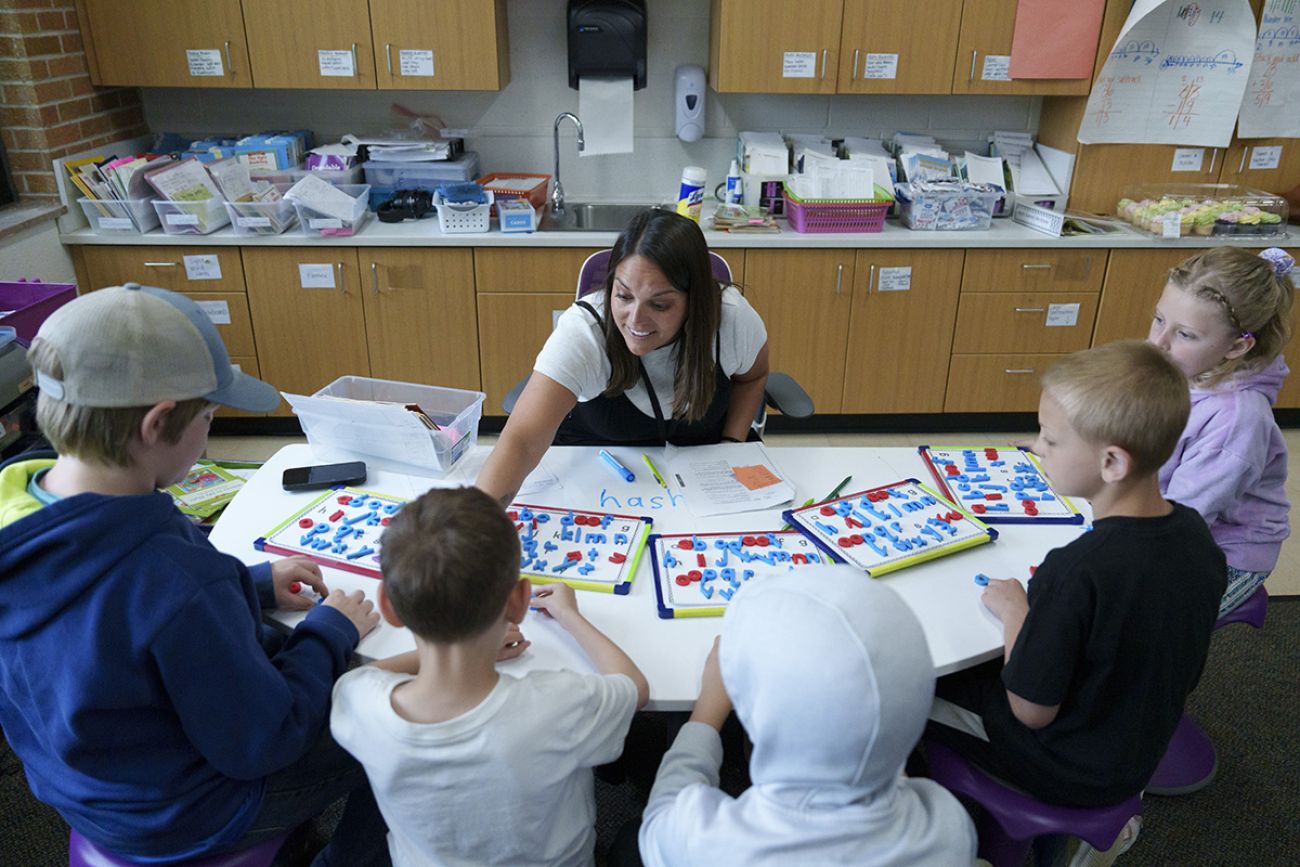 Becca Bradley sits at a table while interacting with students.