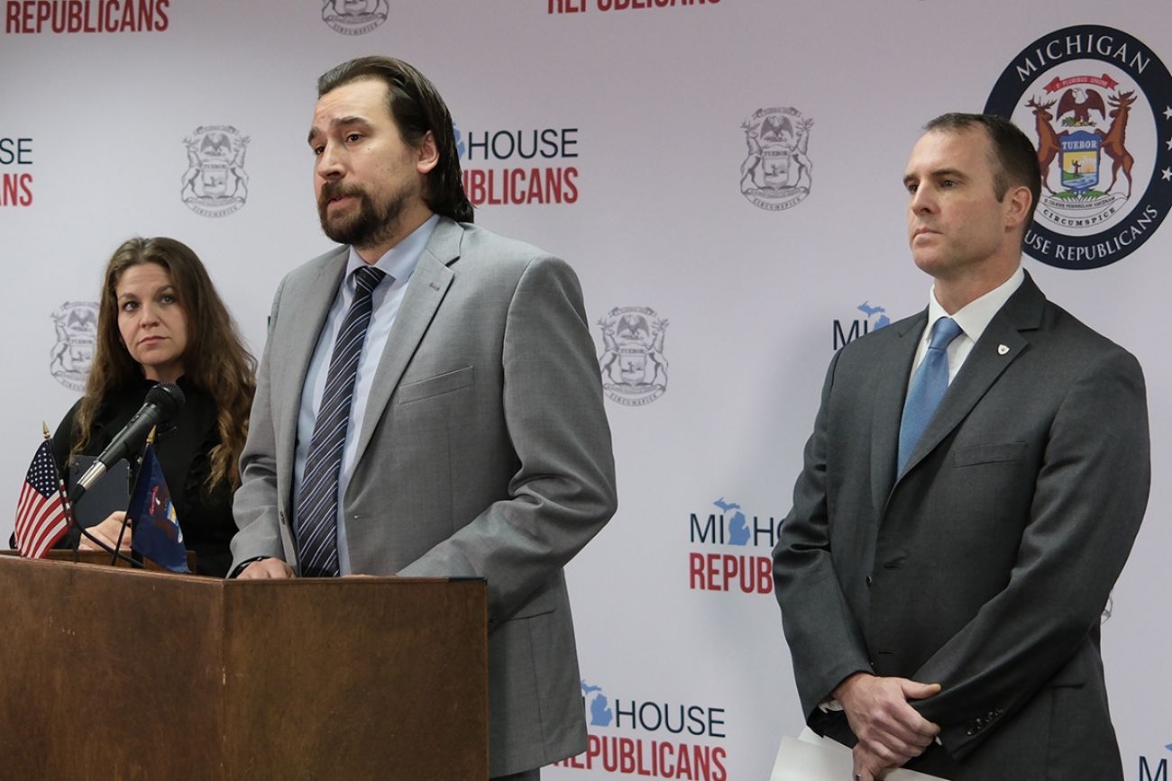 Michigan Rep. Brad Paquette is at a podium. Sen. Thomas Albert stands behind him.