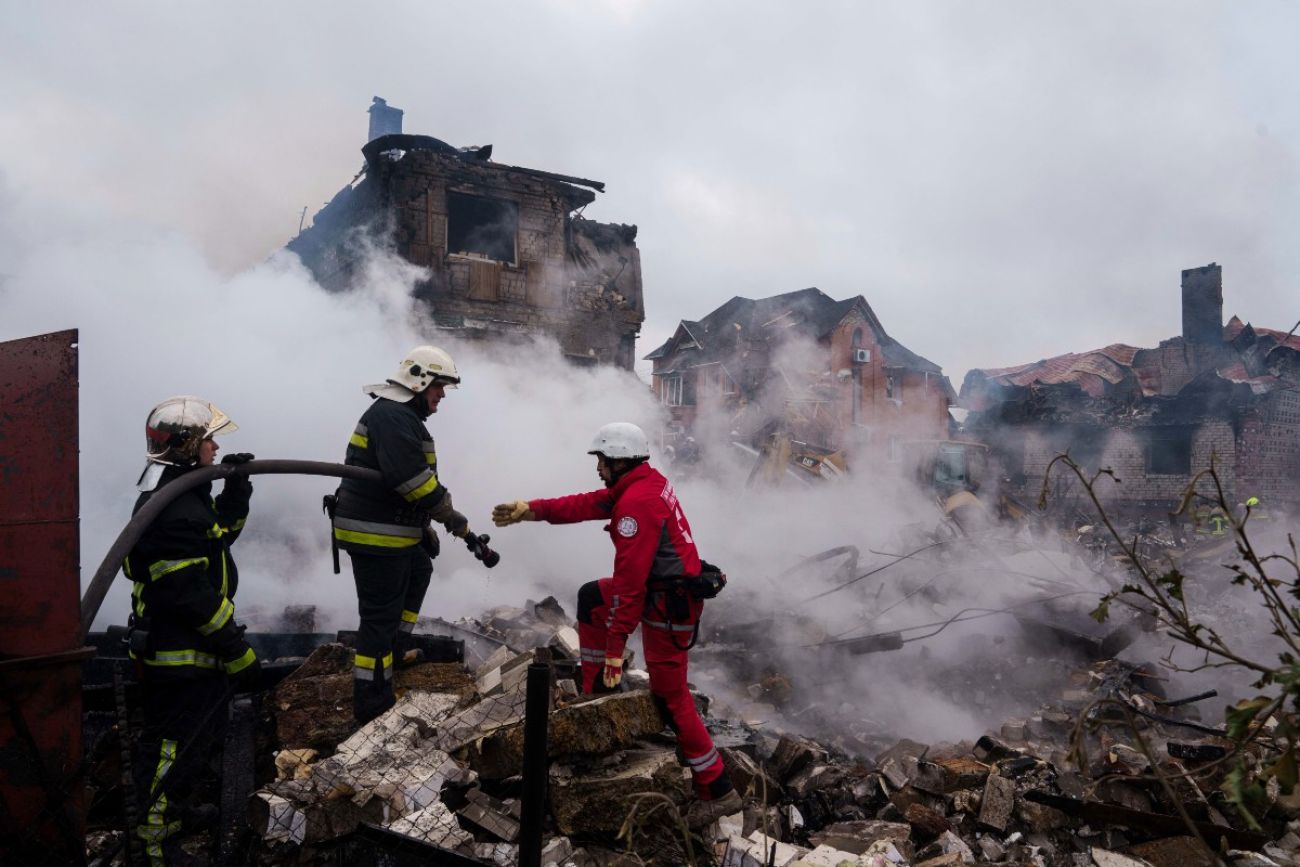Three men stand in front of smoking wreckage