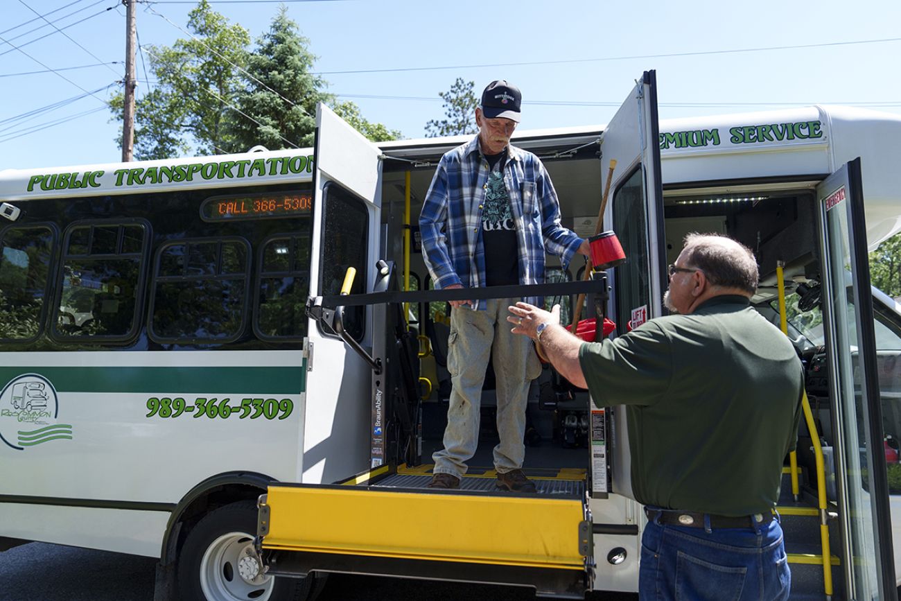 Jesse Smith on a lift of a bus. The driver stands next to the lift.