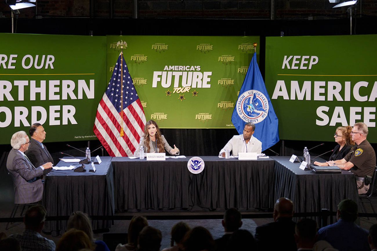 US Department of Homeland Security Secretary Kristi Noem with other officials sitting on a table.