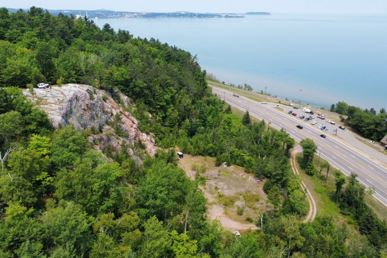 A rock cliff is seen next to a roadway and beyond that Lake Superior