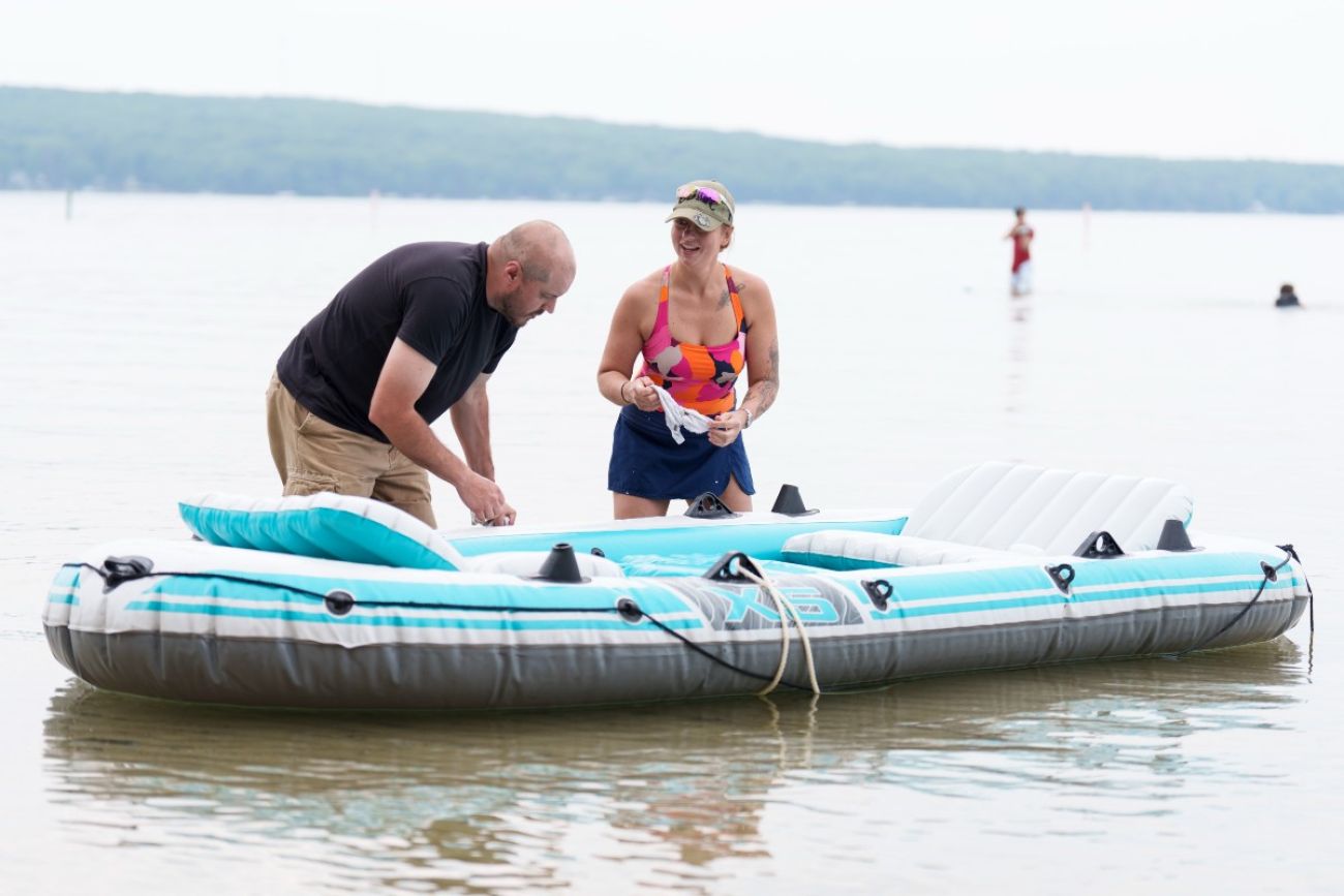 Two people laugh while standing in a lake working on cleaning off a floating raft