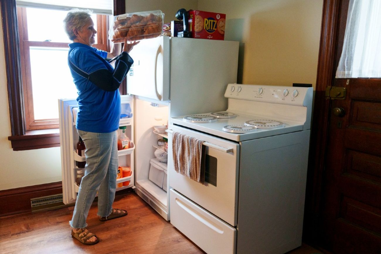 A woman places a plastic box full of croissants on top of a refrigerator