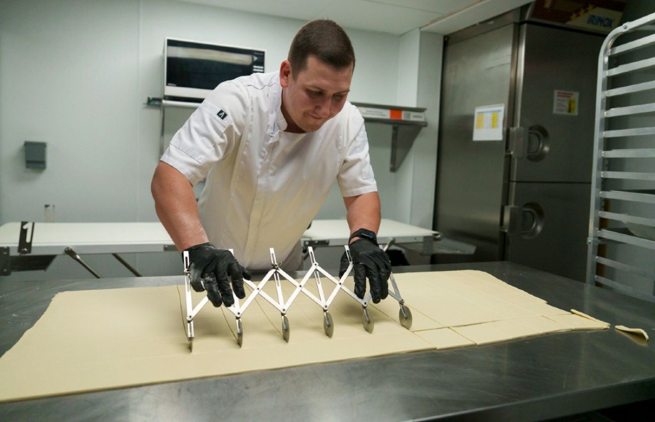Man cuts pastry dough in kitchen
