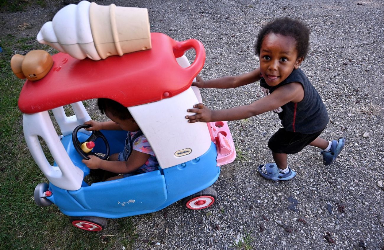 A child pushes another child around in a toy car