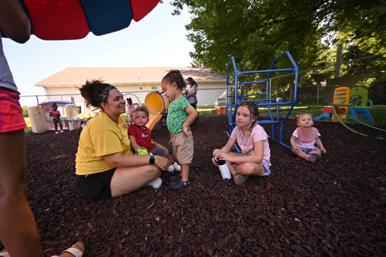 Children and adults sit on the ground at a playground