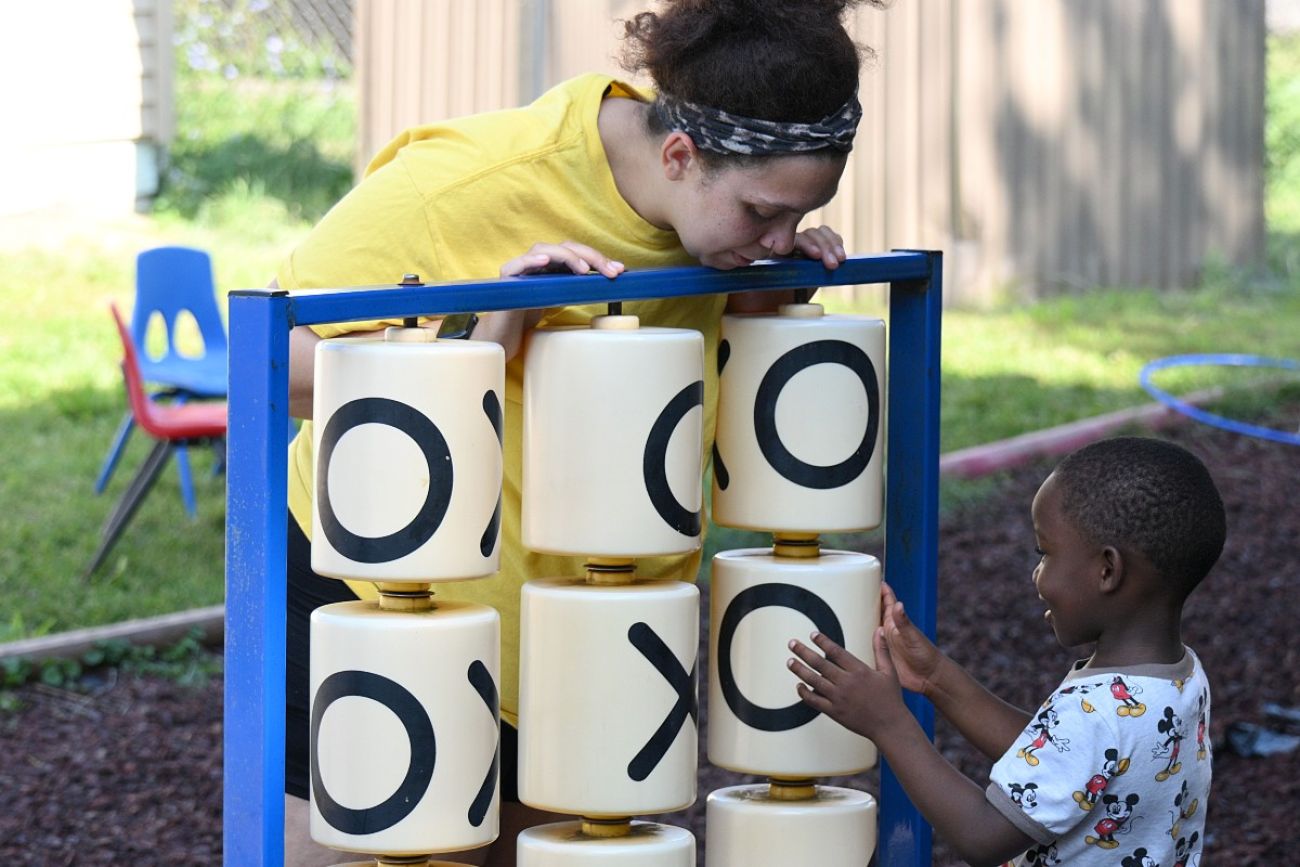 An adult looks over the top of an oversized tic-tac-toe game while a child plays the game