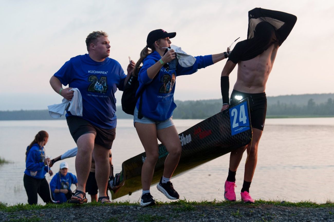 Two women help a canoe racer take his shirt off as he portages during a race