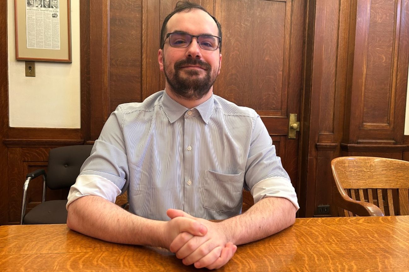 A man poses for a photo while sitting at a table in a conference room