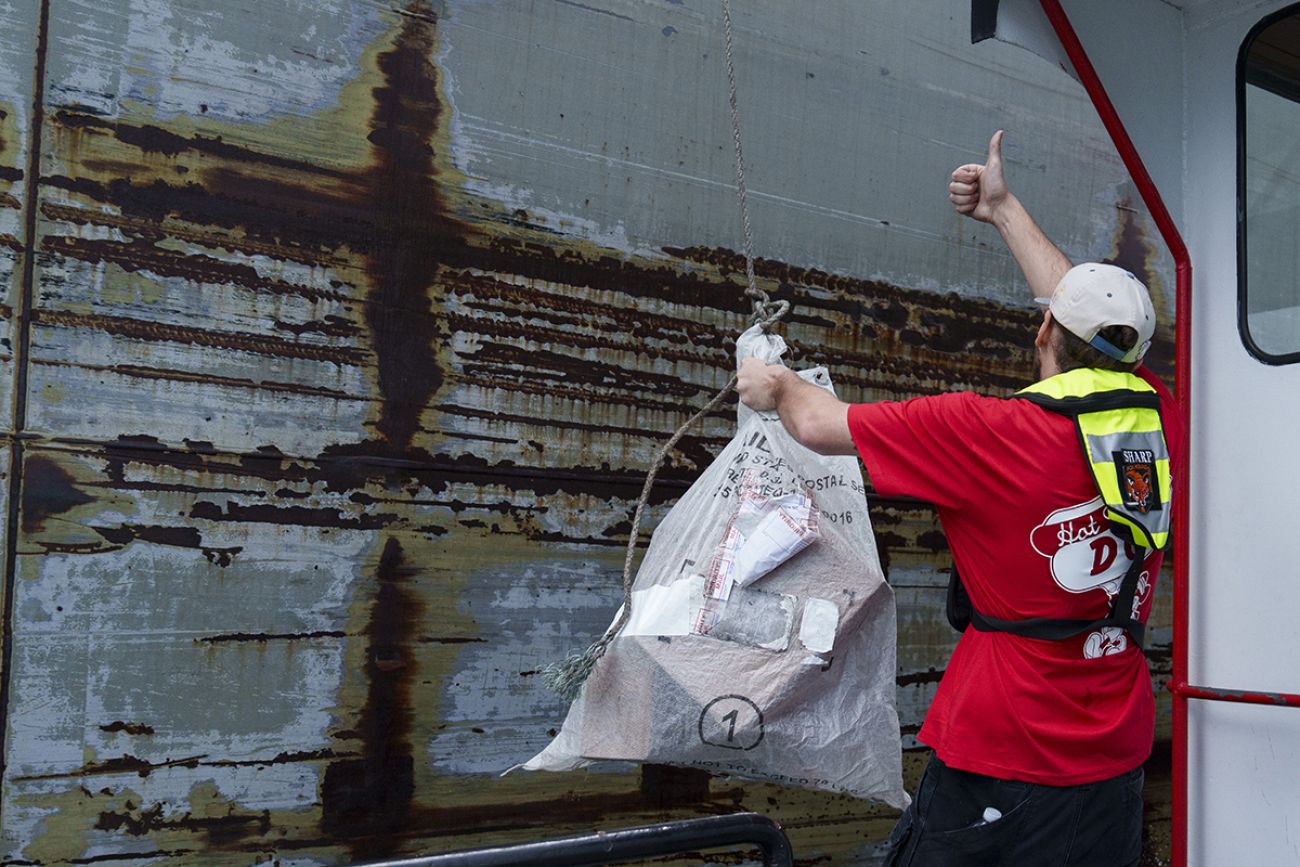 Shipmate JC Sharp holds a bag of mail with one hand and gives a thumbs-up with the other hand.
