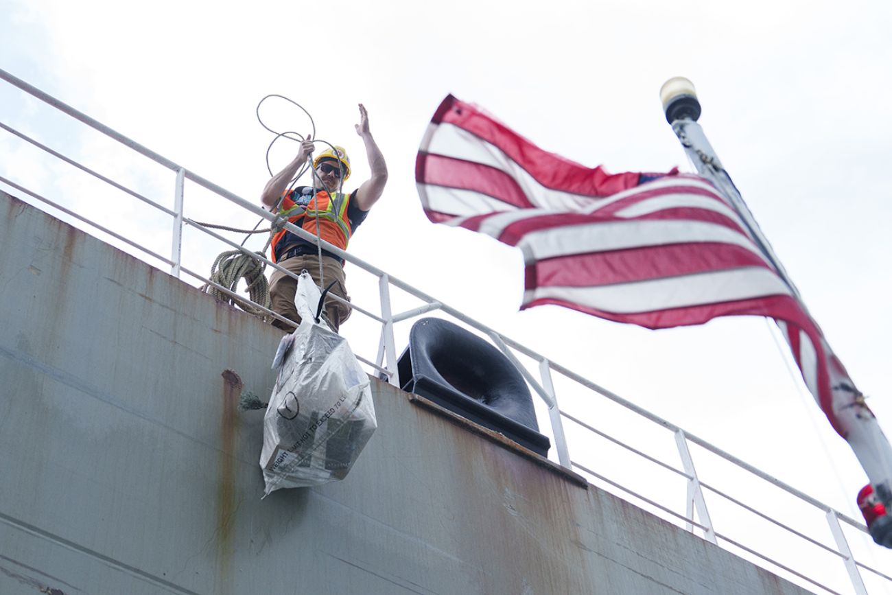 A crew member is on the edge of the boat as he pulls up a bag of mail.
