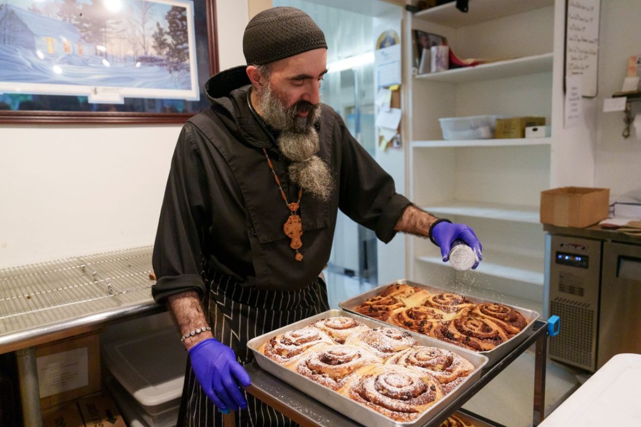 A man sprinkles powdered sugar over panfuls of pastries