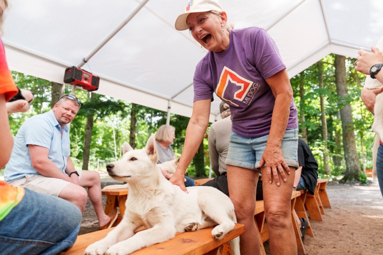 A woman pets a dog that is sitting on a bench while other people sitting around her look on